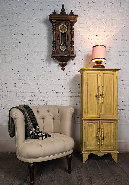 istock Beige armchair, yellow cupboard, pendulum clock and illuminated table lamp 547411830