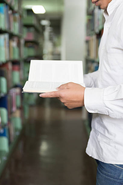 istock man reading book in aisle in library 547414952