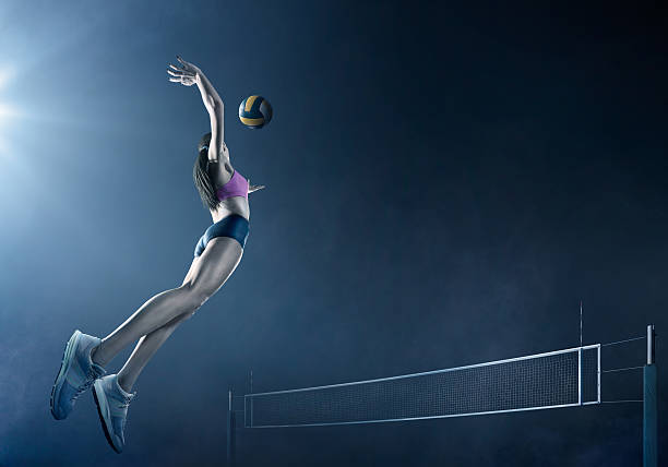 Volleyball: Beautiful female player in action Beautiful female volleyball player performs an emotional game moment on the dark foggy background with net. She is wearing an unbranded sports cloth. womens field event stock pictures, royalty-free photos & images