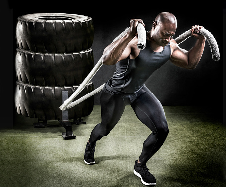 Muscular athlete pulling sled of large tires.