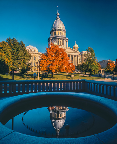 Springfield Illnois Capitol Building surrounded by autumn maple trees and fountain reflection in the foreground