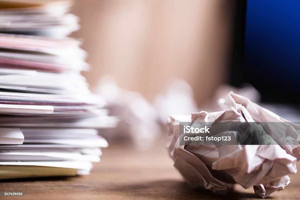 Large stack of files, paperwork. Close-up. Desk, office. Nobody. Large stack of multi-colored files and paperwork lie on an office desk.   Many crumpled papers, trash to side.  Laptop in background.  Copyspace at right.  No people. Bureaucracy Stock Photo