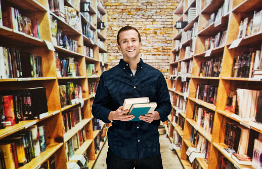 Cheerful bookseller standing in libraryhttp://www.twodozendesign.info/i/1.png