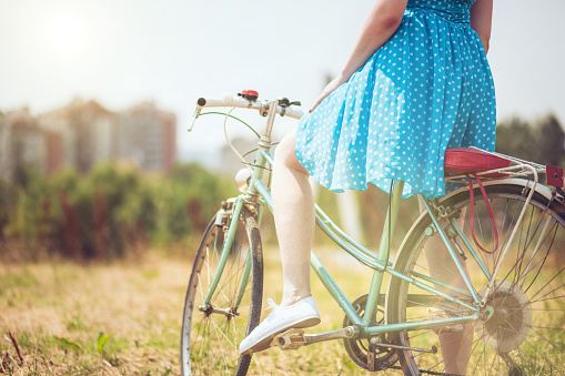 Back view of girl in stylish blue dress sitting on old blue bicycle, in the suuny meadow.