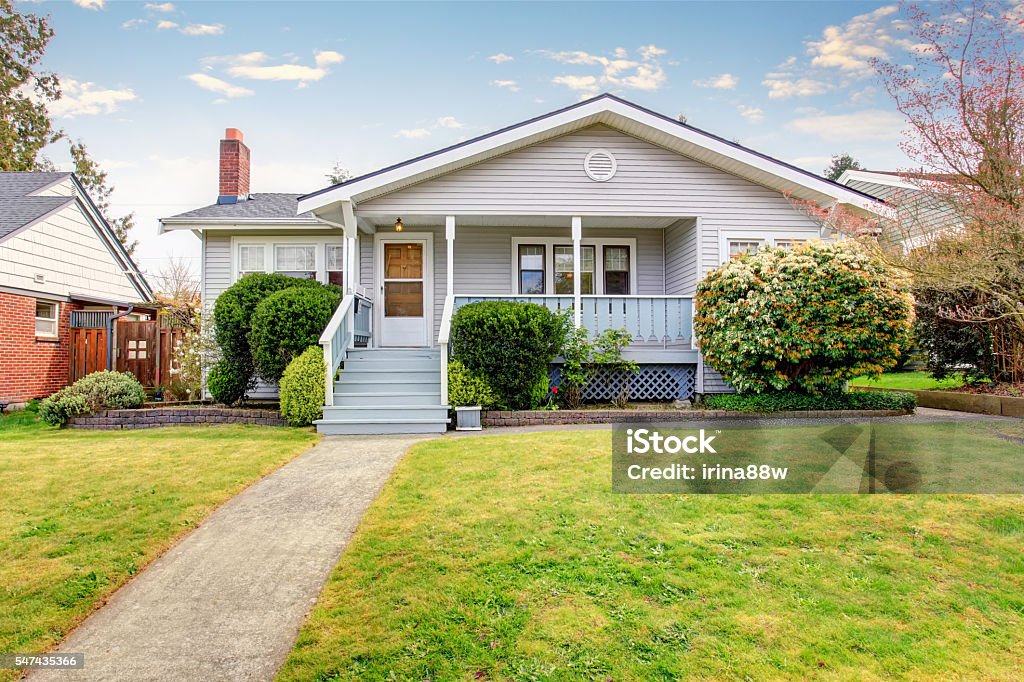 Beige siding house exterior with covered porch. Beige siding house exterior with covered porch and trimmed bushes in front. View of soft blue staircase with narrow walkway. House Stock Photo