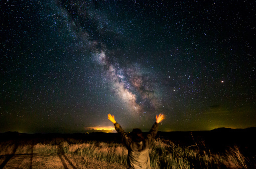Self-portrait under the milky way in the Badlands of South Dakota. A storm lights up the horizon with intense flashes of lightning. Long exposure astrophotography.  