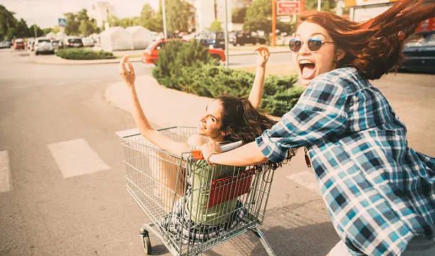 Two young girls having fun with a shopping cart on the street.