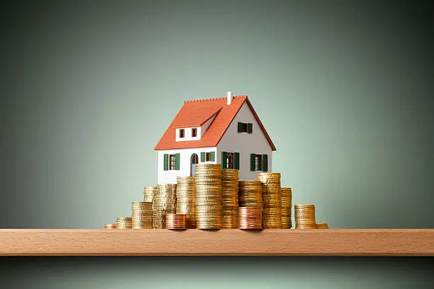 Miniature model house standing on a stack of coins.