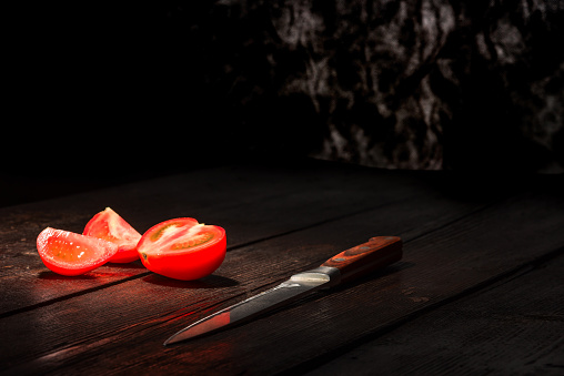 Red tomato and knife on the dark wooden surface.