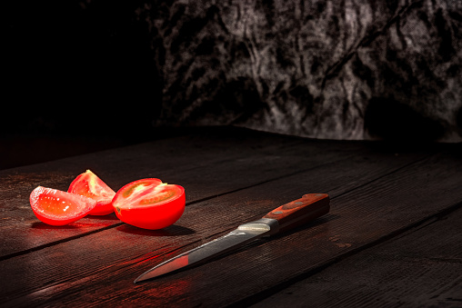 Red tomato and knife on the dark wooden surface.