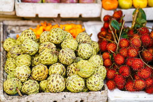 Asian street farmer market selling fresh fruit in Hoi An, Vietnam. Cherimoya and rambutan. Yellow and red colors.