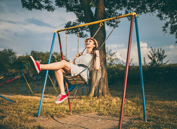 day in the park a beautiful young latin woman with long hair sitting on the swing, she wears a skirt, sweater and hat, lifestyle and beauty