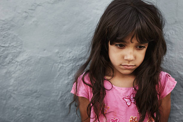 istock Unhappy little girl standing against grey wall 547511806