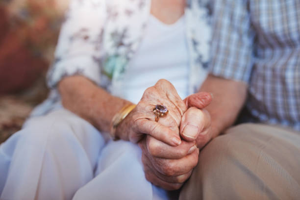 Elderly couple holding hands Cropped shot of elderly couple holding hands while sitting together at home. Focus on hands. couple holding hands stock pictures, royalty-free photos & images
