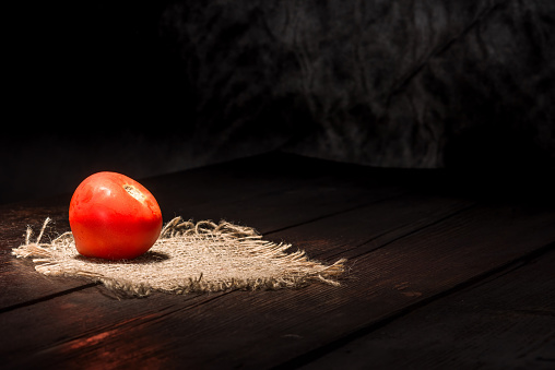 Red tomato on the dark wooden surface.