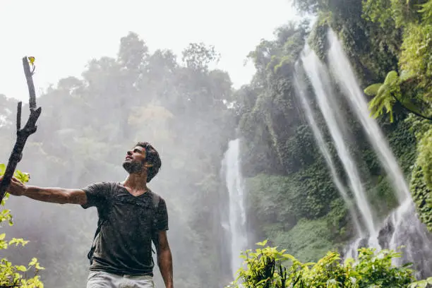 Vector illustration of Young man standing near a waterfall in forest