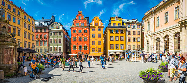 Stockholm Stortorget tourists in medieval square colourful houses restaurants Sweden Stockholm, Sweden - July 9, 2016: Crowds of tourists and locals enjoying the summer sunshine beneath the colourful townhouses and quaint restaurants of historic Stortorget, Great Square, the iconic landmark plaza on Gamla Stan in the heart of Stockholm, Sweden's vibrant capital city. Composite panoramic image created from six contemporaneous sequential photographs. stortorget stock pictures, royalty-free photos & images