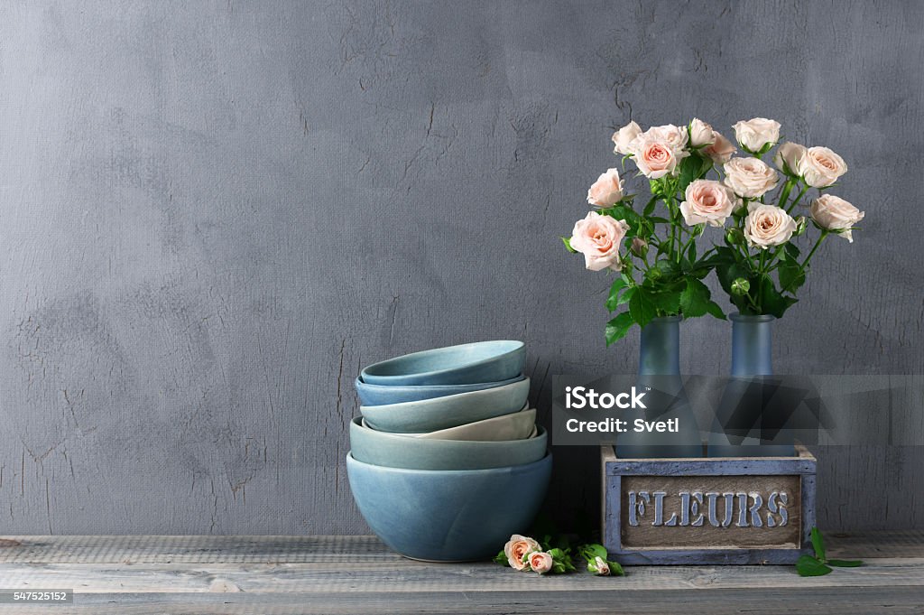 Crocery and roses bouquet Stack of blue handmade ceramic bowls and pink roses bouquet in rustic vase against dark gray wall. Interior Decor Stock Photo