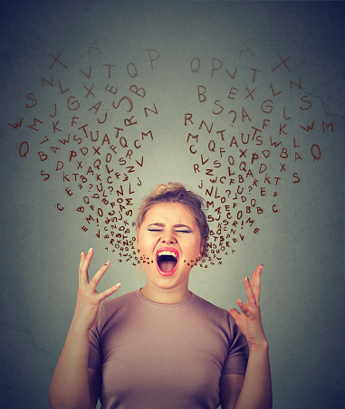 portrait angry woman screaming, alphabet letters coming out of open mouth, isolated gray wall background. Negative human face expressions, emotion, reaction. Conflict, confrontation concept
