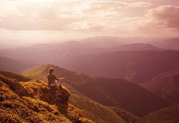 Woman doing yoga on a rock overlooking the mountains at sunset.