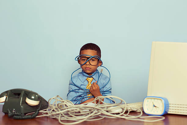 Young Boy IT Professional Smiles at Computer with Wire A young IT professional sadly looks over a large pile of tangled internet cables on his desk. He is dressed in a blue shirt, tie and glasses while looking over worked and tired in front of light blue backround. Retro styling.  overworked funny stock pictures, royalty-free photos & images