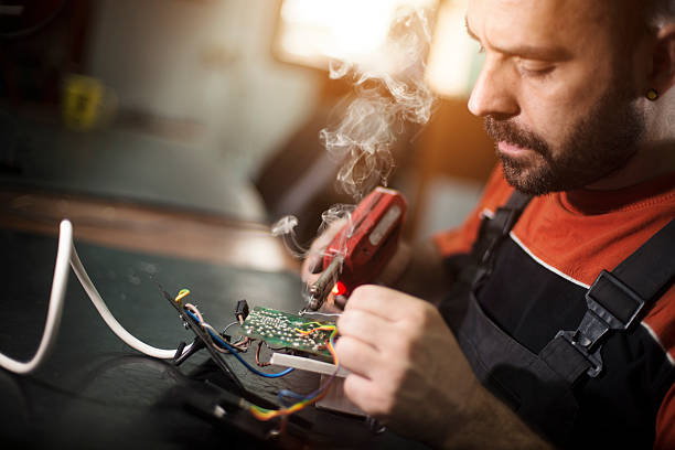 Repairman working in workshop and soldering electric board