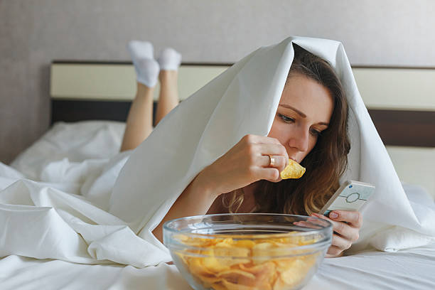 chica comiendo papas fritas en la cama y viendo noticias por teléfono - raw potato red potato red vegetable fotografías e imágenes de stock