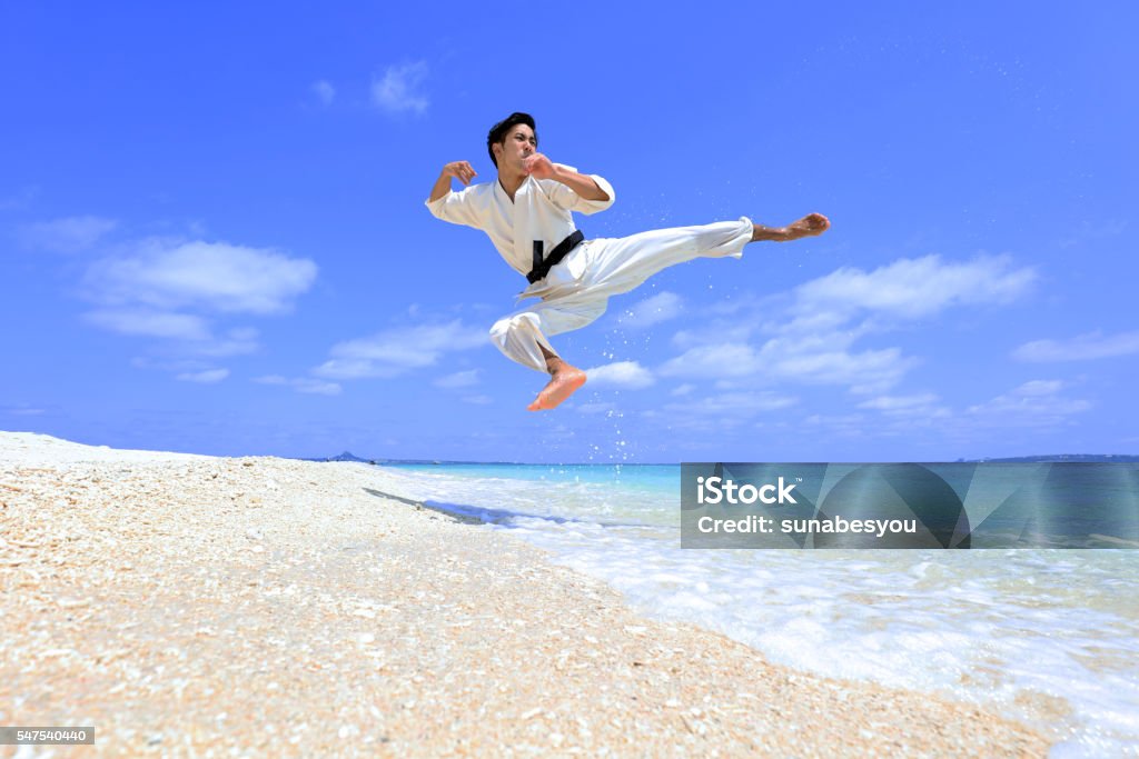 Flying Beach Karate Kick. Young adult man with black belt practicing a Kata on the beach on a sunny day. Karate Stock Photo