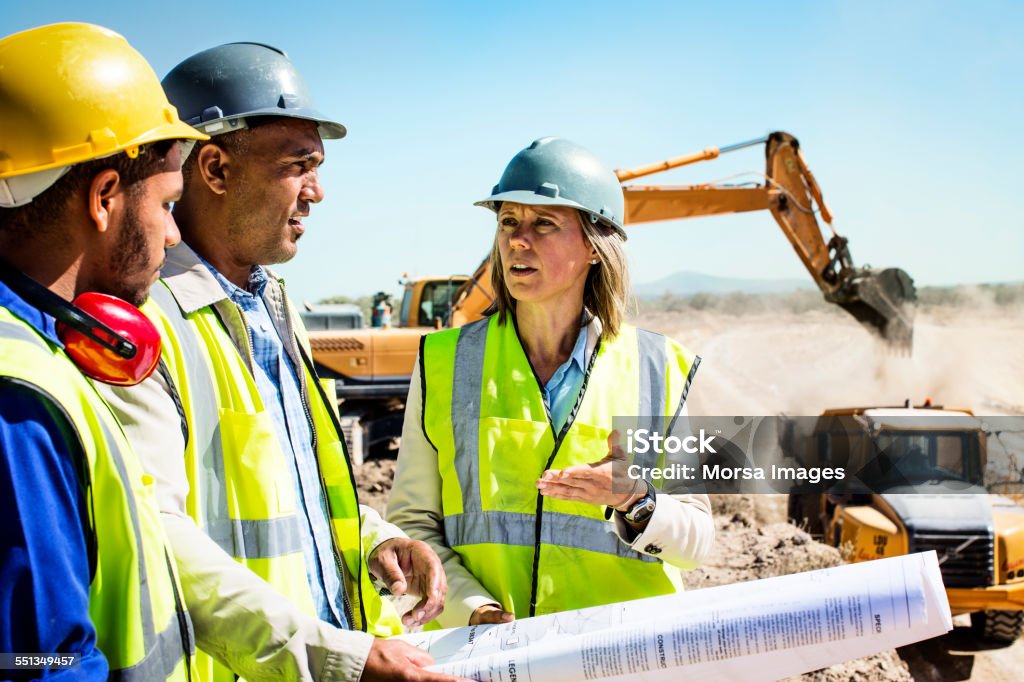 Construction team planning at quarry Architects and worker discussing over blueprint at quarry against clear sky Mining - Natural Resources Stock Photo