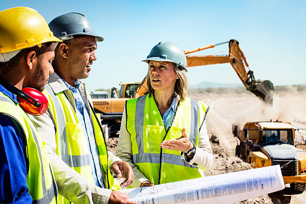 Construction team planning at quarry Architects and worker discussing over blueprint at quarry against clear sky backhoe photos stock pictures, royalty-free photos & images