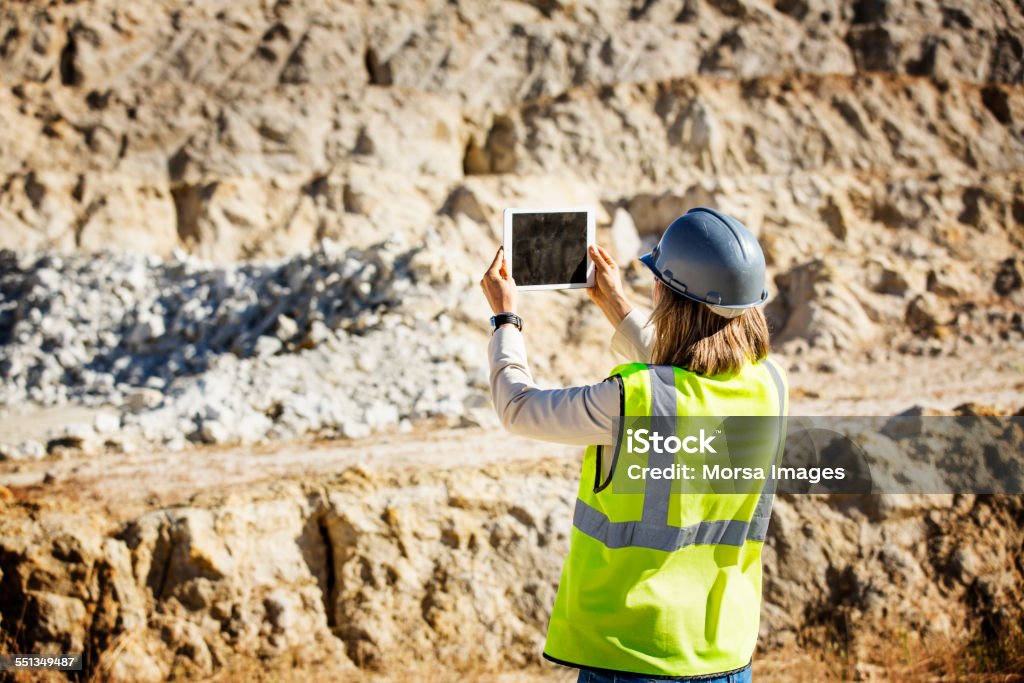 Female architect photographing quarry Rear view of female architect in protective workwear photographing quarry through digital tablet Mining - Natural Resources Stock Photo