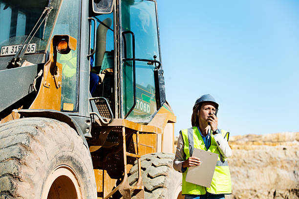 Architect using walkie-talkie at quarry Female architect using walkie-talkie by bulldozer at quarry against clear sky construction vehicle stock pictures, royalty-free photos & images