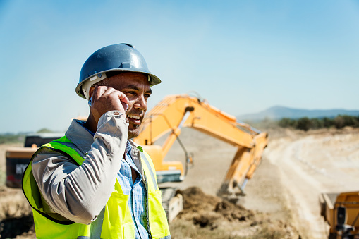 Male architect using mobile phone with bulldozer in background at quarry