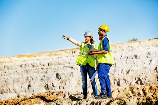 Top view shot of two industrial  workers wearing reflective jackets standing on mining worksite outdoors using digital tablet, copy space