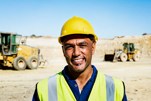 Happy quarry worker at construction site Portrait of happy quarry worker with bulldozers in background at construction site miner photos stock pictures, royalty-free photos & images