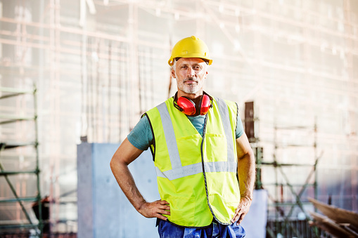 Portrait of confident male architect standing with hands on hips at construction site