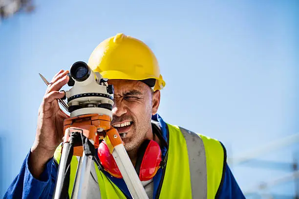 Male architect examining construction site through theodolite against clear sky