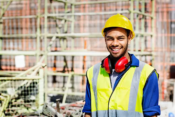 Portrait of happy construction worker in protective workwear standing at site