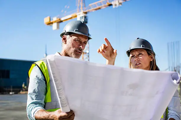 Female architect discussing over blueprint with male colleague at construction site