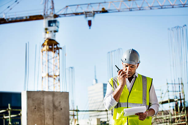Architect using walkie-talkie at construction site Architect using walkie-talkie while reading document at construction site walkie talkie photos stock pictures, royalty-free photos & images
