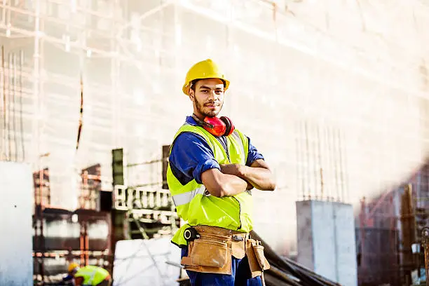 Portrait of confident construction worker in protective workwear standing arms crossed at site