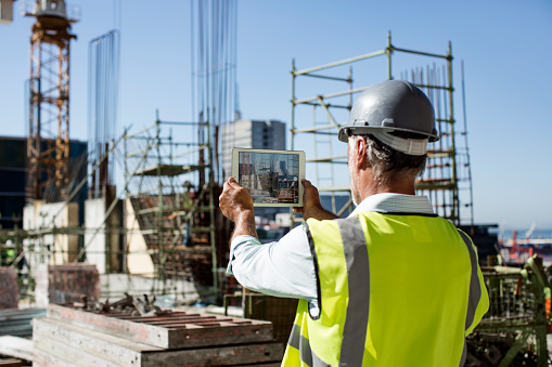 Rear view of male architect photographing construction site through digital tablet