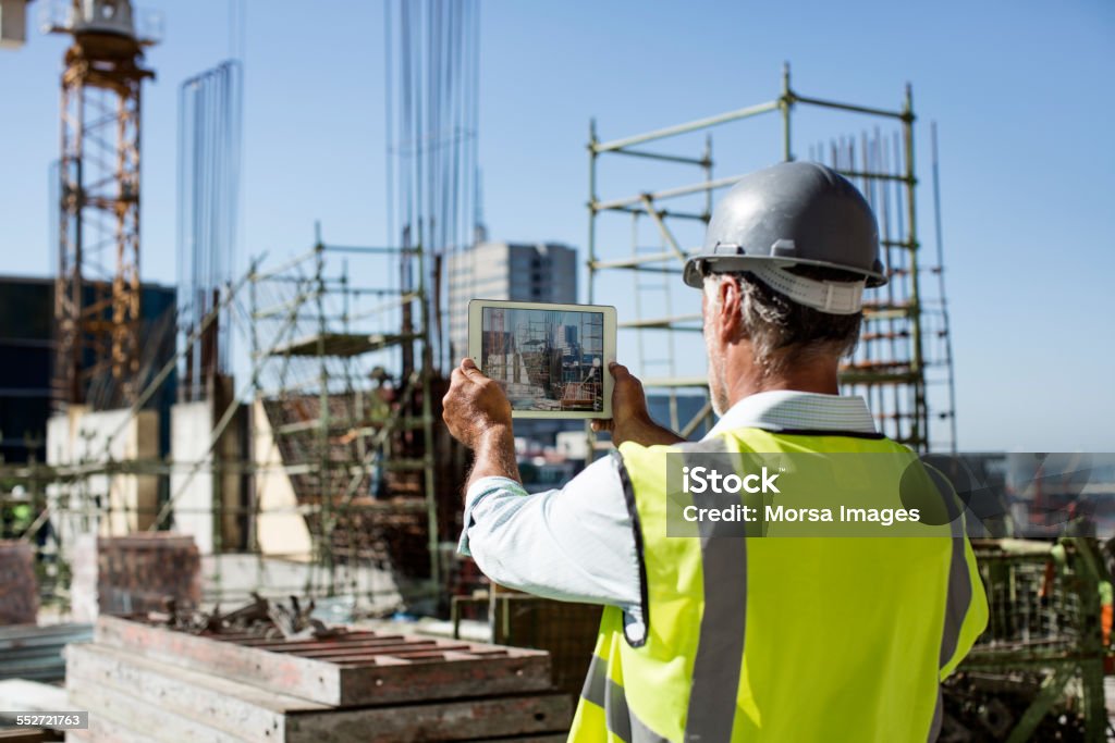 Male architect photographing construction site Rear view of male architect photographing construction site through digital tablet Construction Site Stock Photo