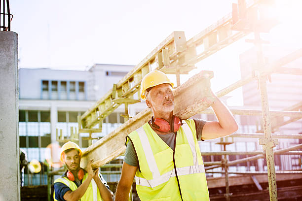 construction workers carrying plank at site - rusztowanie strój zdjęcia i obrazy z banku zdjęć