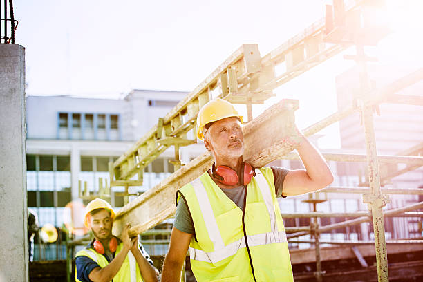 construction workers carrying plank at site - architecture vibrant color bright built structure imagens e fotografias de stock