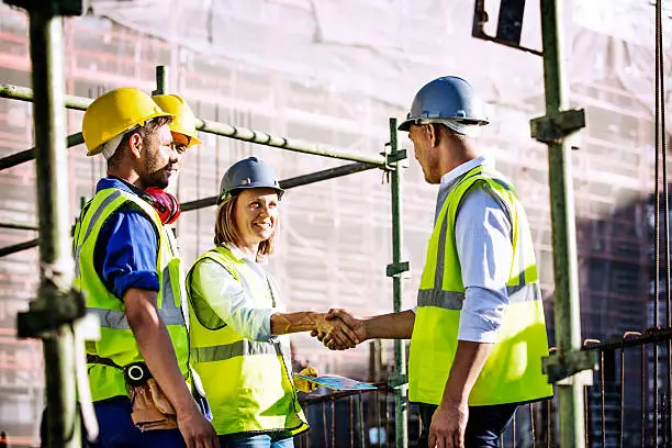 Male and female architects shaking hands at construction site