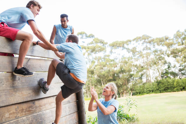 Teammates helping man over wall on boot camp obstacle course  obstacle course stock pictures, royalty-free photos & images