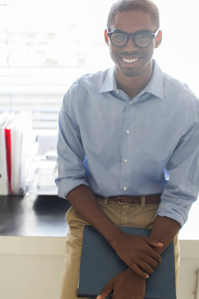 portrait d’un jeune homme souriant portant des lunettes et une chemise bleue appuyée sur un bureau au bureau - 24229 photos et images de collection