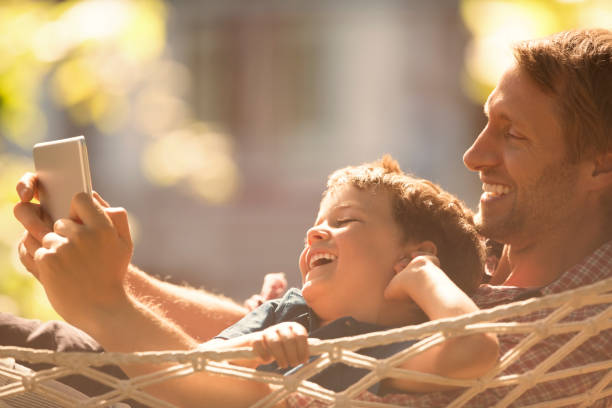 Father and son using digital tablet in hammock  hammock men lying down digital tablet stock pictures, royalty-free photos & images