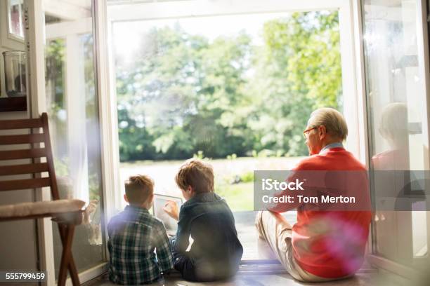Grandfather And Grandsons Relaxing In Doorway Stock Photo - Download Image Now - Senior Adult, Using Computer, Rear View
